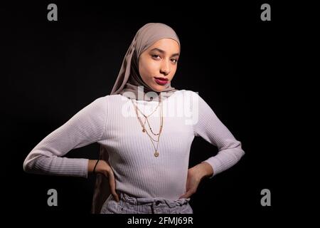 Modisch selbstbewusste muslimische Frau im Hijab stehen und betrachten Kamera im dunklen Studio Stockfoto