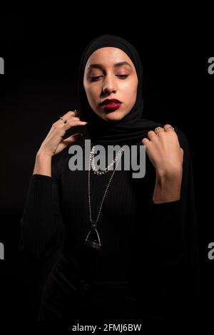 Attraktive junge islamische Frau in schwarzem Outfit und Hijab sanft Nach unten schauen Stockfoto