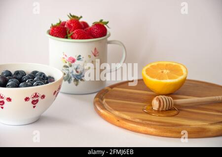 Gesunde Beerenfrüchte mit Honig und Zitrone auf weißem Hintergrund Stockfoto