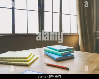 Schreibtisch mit Papieren, Notizbüchern und Stift in der Nähe des Fensters. Stockfoto