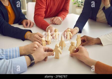 Büroteam von Menschen, die an einem Tisch sitzen und im Kreis hölzerne Figuren von Menschen angeordnet. Stockfoto