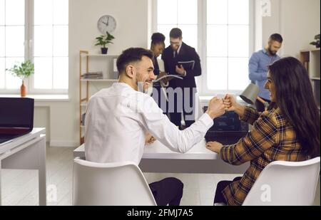Zwei Geschäftsleute oder Kollegen, die einen Deal und eine Faust machen Am Bürotisch sitzend, stolperte es Stockfoto