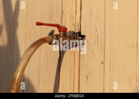 Der Wasserhahn ragt aus der Wand des Hauses. Eiserner Wasserhahn mit rotem Griff und Schlauch. Stockfoto