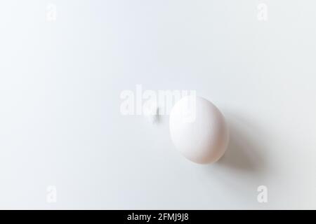 Ein weißes Ei und eine Feder auf weißem Hintergrund mit Kopierfläche. Blick von oben auf isolierte weiße Eier und Federn. Konzept des Minimalismus. Stockfoto