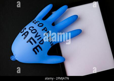 Aufgeblasster blauer Latex-OP-Handschuh auf schwarzem Hintergrund. Covid Safe wieder öffnen. Öffnen Sie den Text, der auf einem medizinischen Handschuh geschrieben ist. Neuer Normalwert Stockfoto