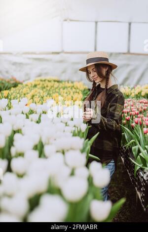 Junge Gärtnerin, die sich um Blumen aus Tulpen kümmert, die in einem Gewächshaus wachsen. Frühlingsblumen und Blumenzucht. Weicher, selektiver Fokus, Unschärfe-Effekt. Stockfoto