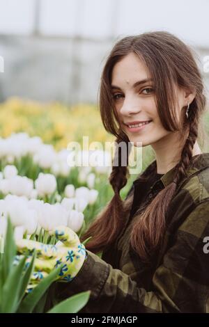 Junge Gärtnerin, die sich um Blumen aus Tulpen kümmert, die in einem Gewächshaus wachsen. Frühlingsblumen und Blumenzucht. Weicher, selektiver Fokus, Unschärfe-Effekt. Stockfoto