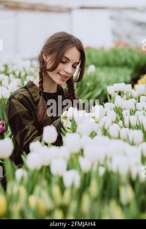 Junge Gärtnerin, die sich um Blumen aus Tulpen kümmert, die in einem Gewächshaus wachsen. Frühlingsblumen und Blumenzucht. Weicher, selektiver Fokus, Unschärfe-Effekt. Stockfoto