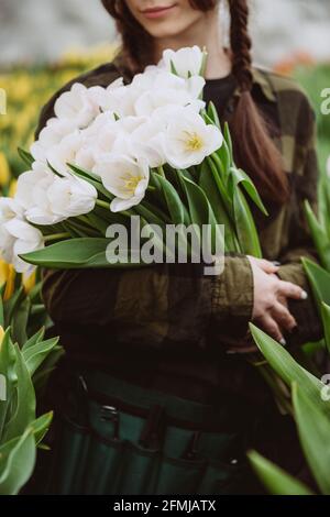 Die junge Gärtnerin hält einen Strauß Tulpen in einem Gewächshaus. Frühlingsblumen und Blumenzucht. Weicher, selektiver Fokus, Unschärfe-Effekt. Stockfoto