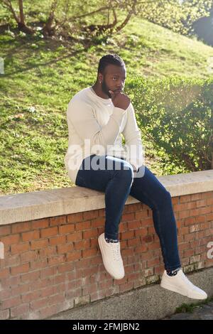 Junger afroamerikanischer Mann, der an einer Wand sitzt. Latino Mann, der durch die Stadt läuft. Hochwertige Fotos Stockfoto