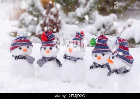 Niedliche kleine Schneemänner mit Hüten und Schals in einem Winterwunderland aus Schnee gruppiert. Stockfoto