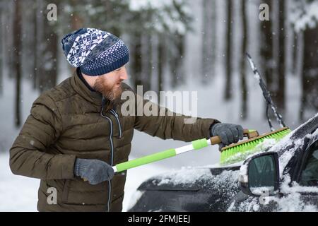 Mann, der an einem Wintertag sein Auto mit einer Bürste vom Schnee säubert. Stockfoto