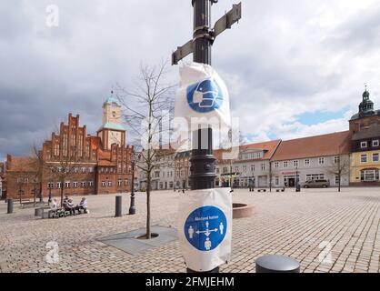 07. Mai 2021, Brandenburg, Wittstock/Dosse: Zerknitterte Folien mit stilisierten Bildern auf einem Laternenpfosten auf dem Platz vor dem Rathaus erinnern die Passanten an die Pflicht, eine Maske zu tragen und auf dem Marktplatz Abstand zu halten. Foto: Soeren Sache/dpa-Zentralbild/ZB Stockfoto