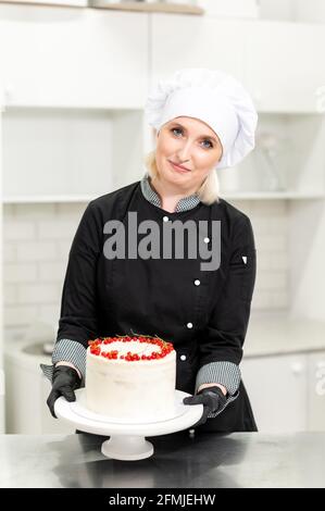 Porträt einer freundlich lächelnden weiblichen professionellen Konditorin, die einen Cupcake umtopping Mit Creme mit einem Gebäckbeutel Stockfoto