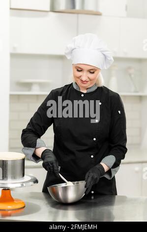 Porträt einer freundlich lächelnden weiblichen professionellen Konditorin, die einen Cupcake umtopping Mit Creme mit einem Gebäckbeutel Stockfoto