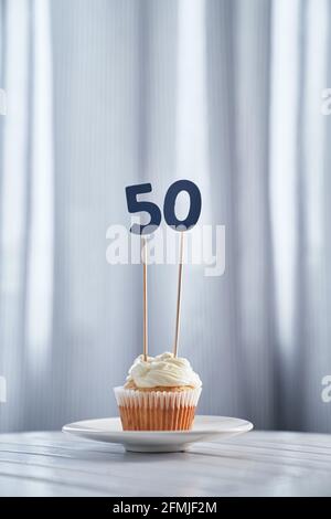 Leckere Vanille hausgemachter Jubiläums-Cupcake oder Muffin mit der Nummer 50 fünfzig auf weißem Teller und hellem Hintergrund. Minimalistisches Geburtstagskartenkonzept. Hochwertige vertikale Fotos Stockfoto