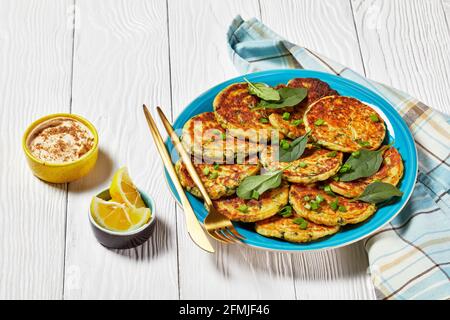 Kichererbsen Spinat Pfannkuchen auf einem blauen Teller auf einem weißen Holztisch mit Hummus in einer kleinen Schüssel Stockfoto