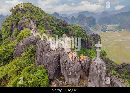 Familie von Touristen auf dem Hintergrund der erstaunlichen riesigen Drachenstatue auf Kalkstein Berggipfel in der Nähe Hang Mua Aussichtspunkt am nebligen Morgen. Beliebt Stockfoto