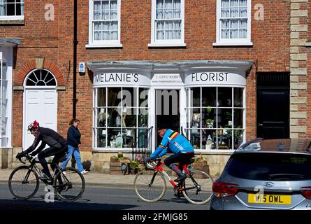 Fahrradfahrer, die an einem Blumengeschäft in der Bridge Street, Tadcaster, North Yorkshire, England, vorbeikommen Stockfoto