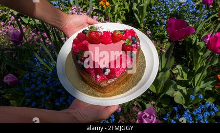 Herzförmiger Kuchen mit Blumen im Hintergrund Stockfoto