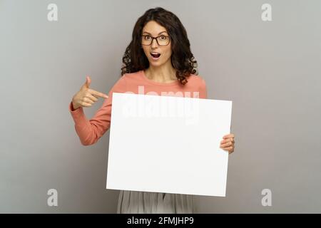 Schockiert und aufgeregt zeigen junge Dame ein leeres Plakat-Banner, das auf einen Platz für die Werbung verweist Stockfoto