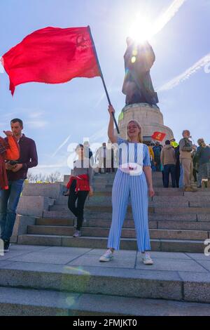 9. Mai 2021, Berlin, am sowjetischen Kriegsdenkmal im Treptower Park (Treptower Ehrenmal), einem Denkmal und gleichzeitig einem Militärfriedhof, gedenken zahlreiche Russen und Deutsch-Russen mit vielen bunten Fahnen des 76. Siegestages am Ende des Zweiten Weltkriegs. Das Denkmal wurde 1949 auf Anweisung der sowjetischen Militärverwaltung in Deutschland errichtet, um die im Zweiten Weltkrieg verstorbenen Soldaten der Roten Armee zu ehren Über 7000 der in den Schlacht um Berlin verstorbenen Soldaten sind hier begraben. Im Bild: Ein Besucher mit der sowjetischen Flagge vor der kolossalen Statue mit Stockfoto