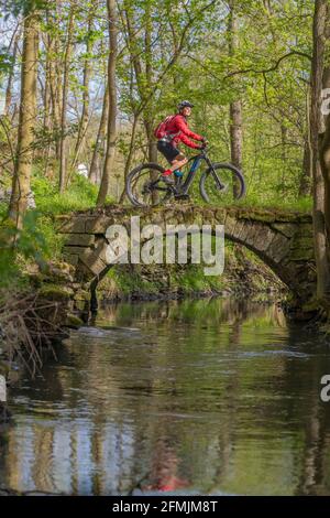 Nette aktive ältere Frau, die im Frühjahr ihr elektrisches Mountainbike entlang des kleinen Flusses Glems bei Stuttgart, Baden-Württemberg, Deutschland, fährt Stockfoto