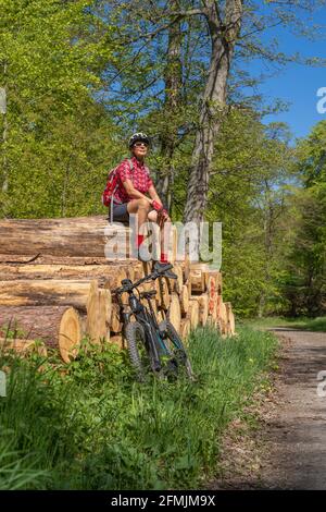 Nette und verbliebene junge ältere Frau, die während einer Radtour in einem Frühlingswald in der Str. auf einem Baumstämmen-Haufen saß und eine Rast hatte Stockfoto
