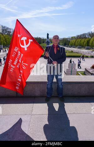 9. Mai 2021, Berlin, am sowjetischen Kriegsdenkmal im Treptower Park (Treptower Ehrenmal), einem Denkmal und gleichzeitig einem Militärfriedhof, gedenken zahlreiche Russen und Deutsch-Russen mit vielen bunten Fahnen des 76. Siegestages am Ende des Zweiten Weltkriegs. Das Denkmal wurde 1949 auf Anweisung der sowjetischen Militärverwaltung in Deutschland errichtet, um die im Zweiten Weltkrieg verstorbenen Soldaten der Roten Armee zu ehren Über 7000 der in den Schlacht um Berlin verstorbenen Soldaten sind hier begraben. Im Bild: Ein Besucher mit sowjetischer Flagge. Weltweite Nutzung Stockfoto