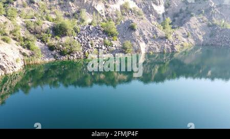 Felsige Ufer des Radon Lake an einem sonnigen Sommermorgen. Luftaufnahme eines alten überfluteten Granitsteinbruchs. Ein malerischer Teich. Stockfoto