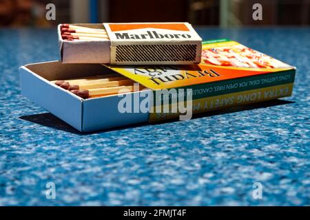 Zwei Kartons mit kurzen und extra langen Streichhölzer, Marlboro und Bryant & May Marken mit Werbung darauf, auf einer melierten blauen Oberfläche. Stockfoto