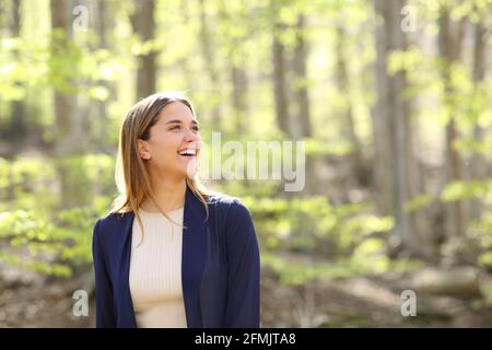Glückliche Frau, die in einem wunderschönen Wald über die Aussicht nachdenkt und lacht Stockfoto