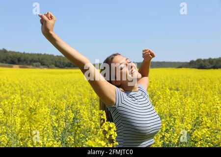 Glückliche Frau, die die Arme in einem gelb blühenden Feld ausstreckt Frühjahrssaison Stockfoto