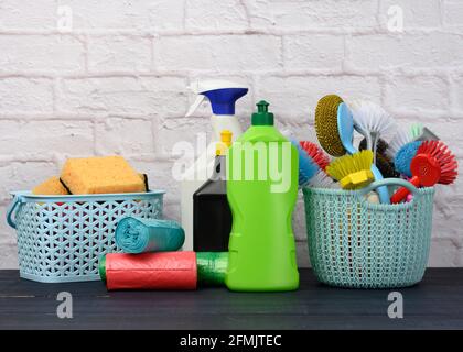 Schwämme, Plastikbürsten und Waschmittelflaschen auf einem blauen Holztisch. Haushaltsreinigungsgegenstände auf weißem Backsteinwand Hintergrund Stockfoto