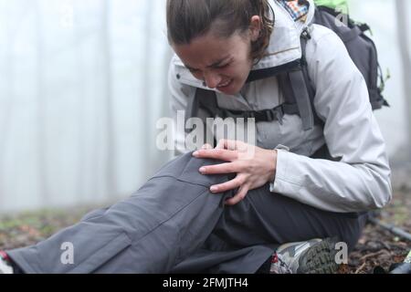 Wanderer beschwerten sich mit gebrochenem Knie, das auf dem Boden saß Ein Wald ein nebliger Tag Stockfoto