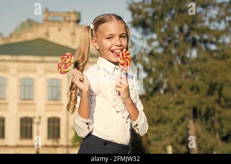 Süßigkeiten machen den Mund glücklich. Kleines Mädchen leckt Süßigkeiten sonnig im Freien. Süßigkeitengeschäft. Lollipop oder Sauger. Zuckerhaltige Leckerbissen. Süßwaren. Essen und Snacks. Süß Stockfoto