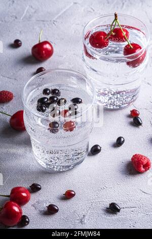 Fresh cold sparkling water drink with cherry, raspberry and currant berries in two transparent glass on stone concrete background, summer diet beverag Stockfoto