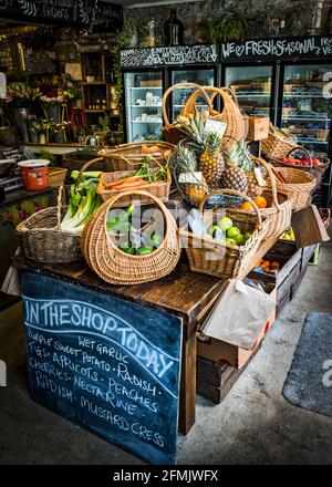 Gemüsehändler in England zeigt seine zentrale Insel mit Obst und Gemüse, die in Körben mit Kühlschränken hinter dem Laden verkauft werden. Stockfoto