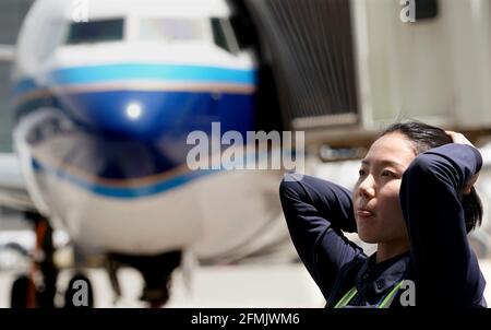 (210510) -- ZHENGZHOU, 10. Mai 2021 (Xinhua) -- Liu Qiqi arrangiert ihre Haare auf einer Wartungsbasis der Henan-Niederlassung von China Southern Airlines in Zhengzhou, der zentralchinesischen Provinz Henan, 30. April 2021. Liu Qiqi ist ein 24-jähriger Mechaniker in der Henan-Niederlassung von China Southern Airlines. Liu Qiqi, der 2019 an der Universität für Zivilluftfahrt in China abschloss, ist ein Blickfang im Team, da sie die einzige Mechanikerin in den fast 200 Mitarbeitern im Bereich Instandhaltung ist.Liu arbeitete in einer traditionell von Männern dominierten Industrie und wurde viel befragt, als sie in den Beruf eintrat. Der Job erfordert harte gr Stockfoto