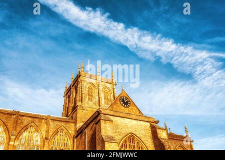 Sherborne Abbey, Dorset, Großbritannien mit dem Turm und der Uhr und einem blauen Himmel mit einem Himmelsweg im Hintergrund. Stockfoto