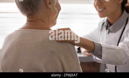 Freundliche junge Therapeutin, die die Schulter einer kranken älteren Frau berührt Stockfoto