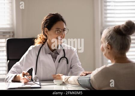 Selbstbewusster hausarzt für lateinische Frauen, der die Spannung einer älteren Patientin misst Stockfoto