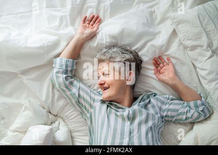 Blick von oben auf eine glückliche ältere Frau im Bett zu Hause, entspannend. Stockfoto