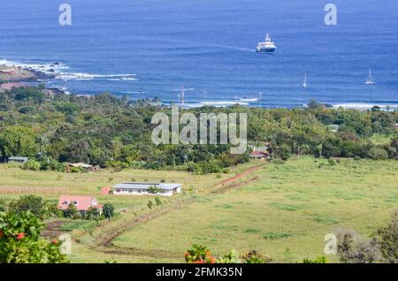 Blick auf einen Bauernhof mit einem bepflanzten Feld am Stadtrand von Hanga Roa, Osterinsel, Chile. Im Hintergrund ist ein vor der Küste verankertes Schiff zu sehen. Stockfoto