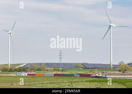 Vorbei Bulk-Containerschiff auf dem Fluss IJssel vor Einer großen Energieproduktionsanlage mit Windenergieanlagen und Sonnenkollektoren in den Niederlanden Stockfoto