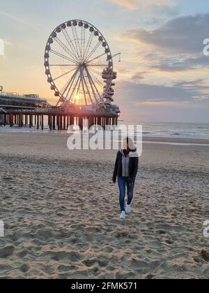 Das Riesenrad der Pier in Scheveningen, Den Haag, Niederlande an einem Frühlingstag, junge Frau am Strand Stockfoto