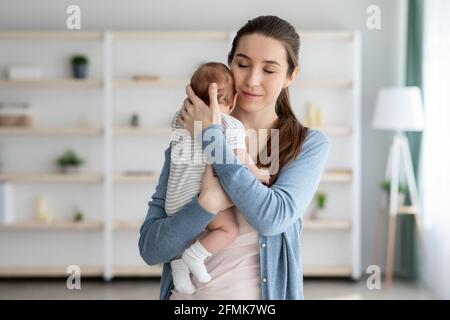 Als MUTTER. Portrait Of Loving Young Woman Zärtlich Umarmt Ihr Neugeborenes Baby, Stehend Mit Geschlossenen Augen, Ruhige Millennial Mama Genießen Ausgaben Stockfoto