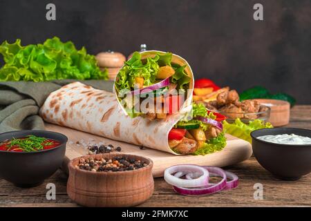 Zwei traditionelle orientalische Shawarma-Gerichte mit Fleisch und Gemüse auf braunem Hintergrund mit Zutaten. Fast Food, schnelle Snacks. Stockfoto