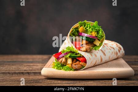Hühnerfleisch, Pommes frites, Gemüse und Salat werden auf braunem Hintergrund in Pita-Brot eingewickelt. Traditionelles Shawarma. Seitenansicht, Kopierbereich. Stockfoto