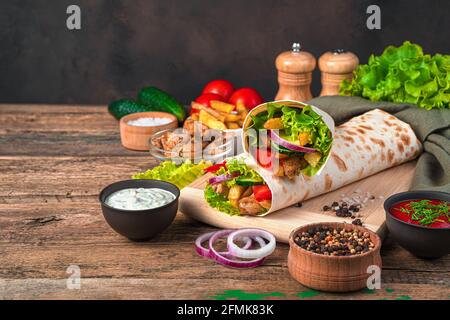 Hühnershawarma mit Pommes frites, Gemüse, Zwiebeln und Salat auf braunem Hintergrund. Seitenansicht, Kopierbereich. Stockfoto